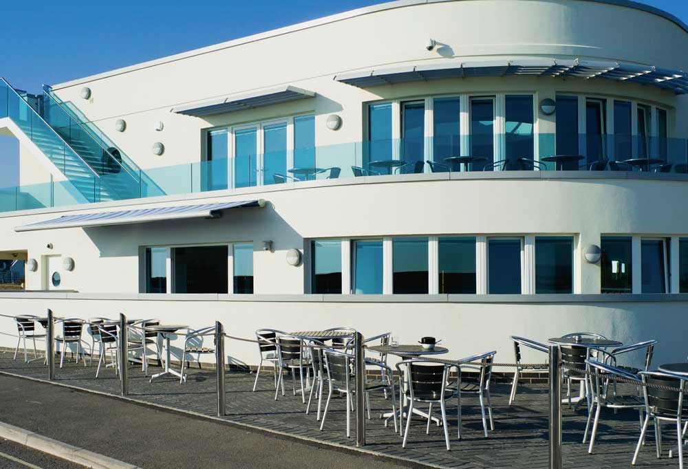 external photo of aluminium windows on a curved building with tables and chairs outside