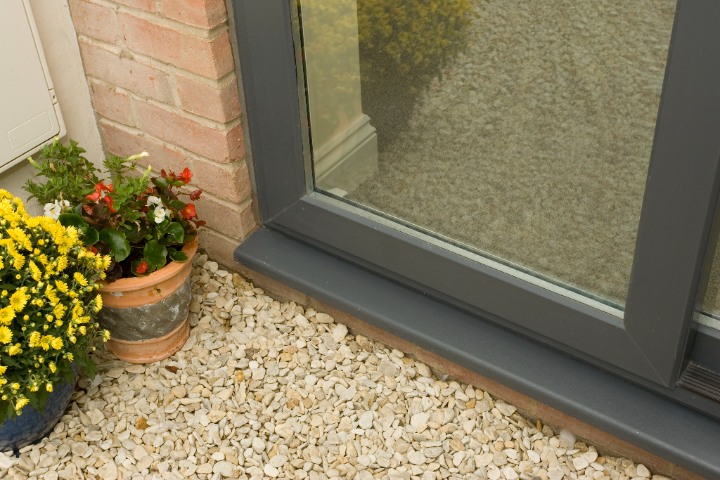 Syncro sliding patio door with grey frame beside a brick wall and decorative potted plants.