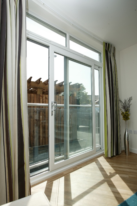 White Syncro sliding patio doors with full-height glass panels and striped curtains in a sunlit living room.